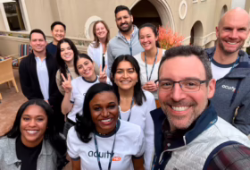 Diverse group of coworkers posing for a group selfie on a sunny rooftop terrace.